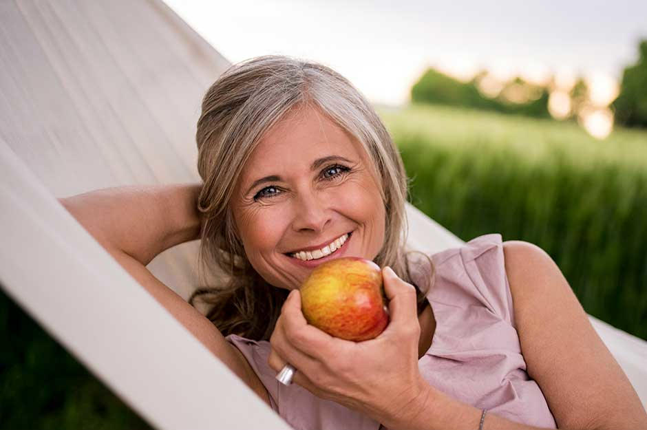 Senior woman smiling outdoors eating an apple on hammock