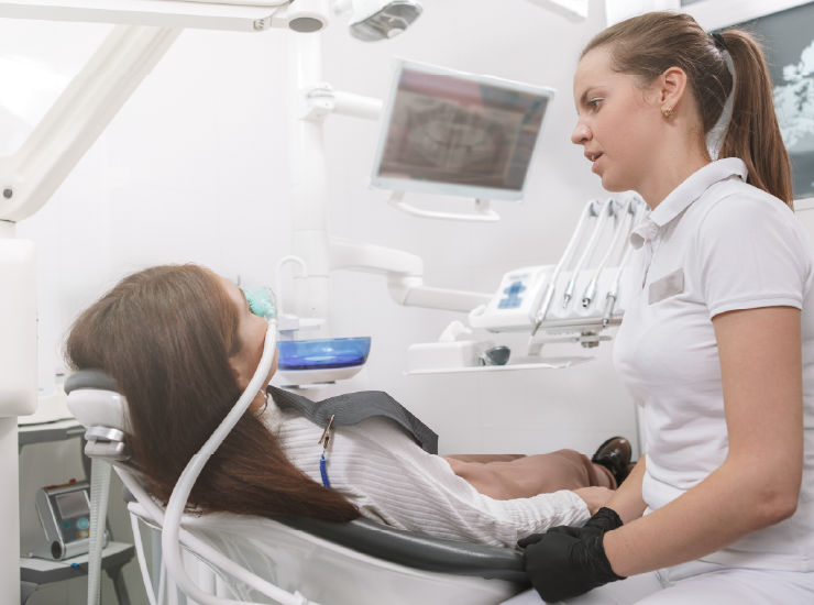 Female patient in dental chair sedation mask. dental assistant talking to her.