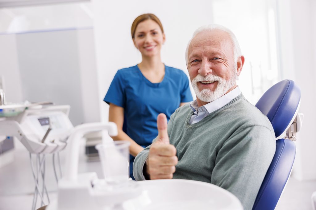 Senior man giving thumbs up in dental chair.