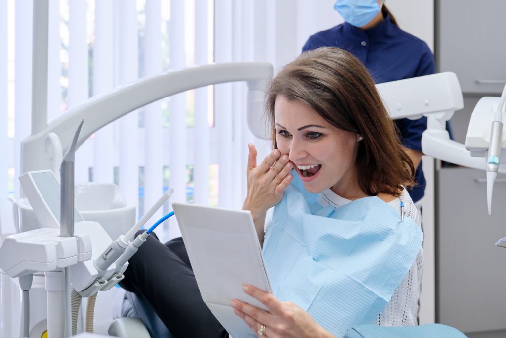 Happy middle aged woman with dentist looking in mirror at teeth.
