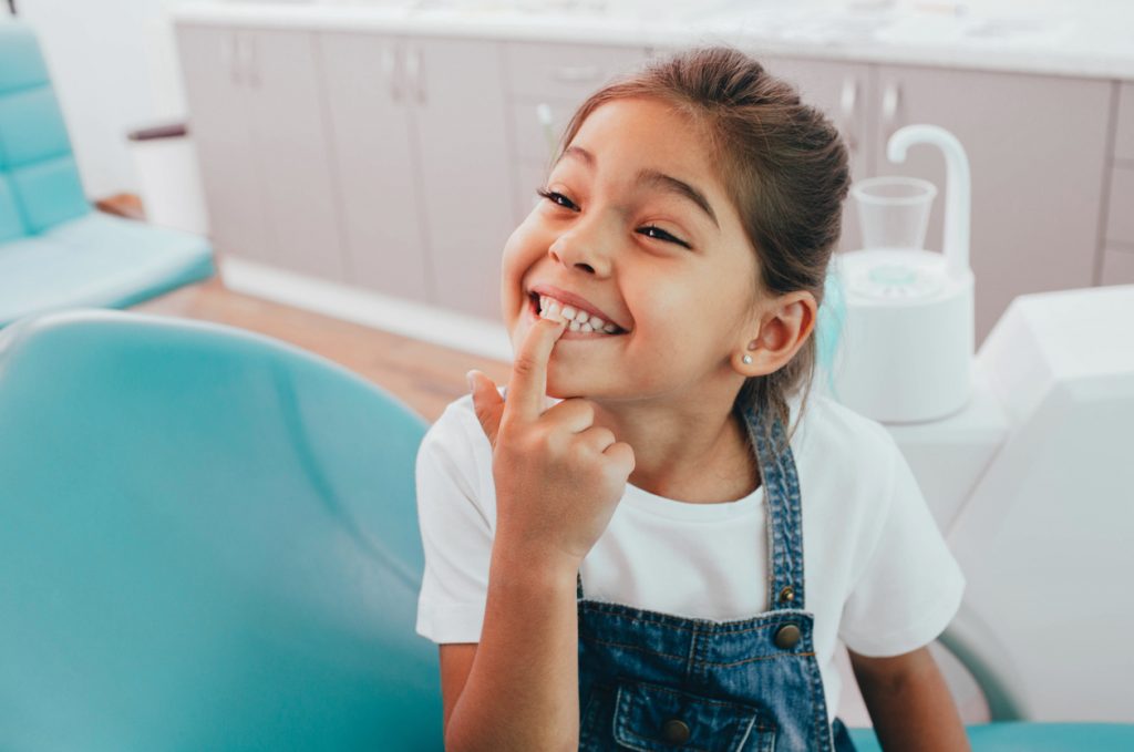 A young girl points to her smile after a frenectomy procedure.