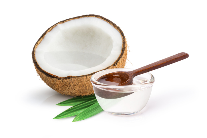 Half a coconut and a glass container of coconut oil with a wood spoon