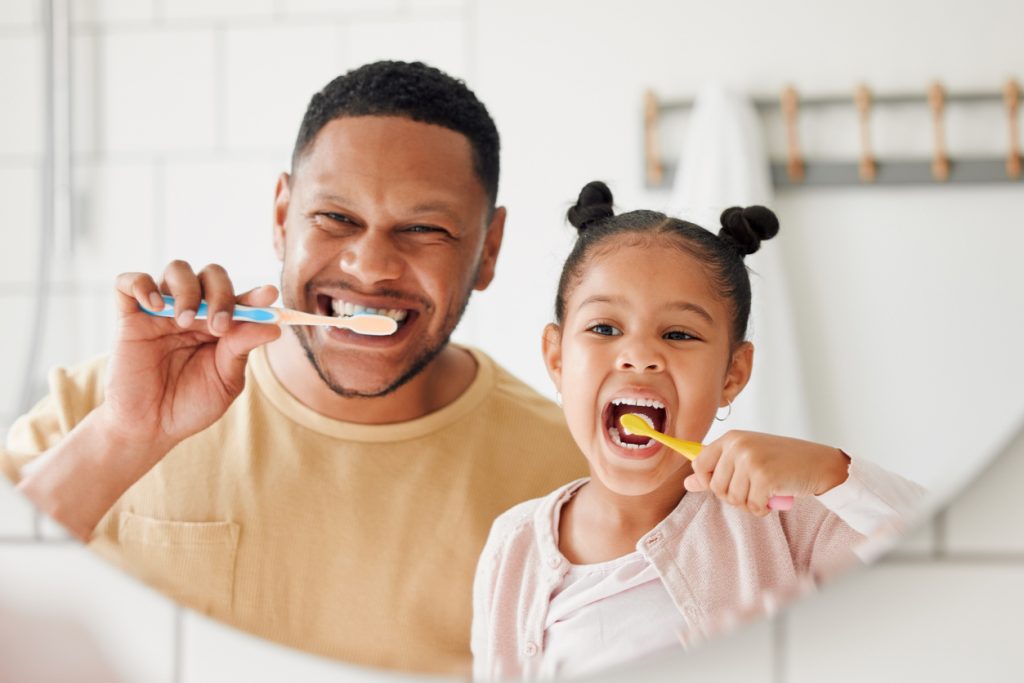 Dad and daughter brushing their teeth while looking in the mirror