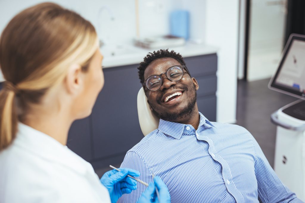 Man sitting in a dental chair smiling at dental hygienist
