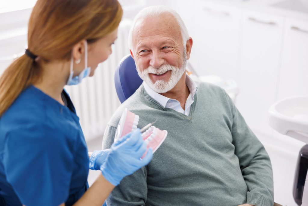 Senior man in dental chair smiling with dental assistant after a procedure