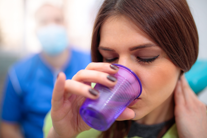 woman swallowing a sedation pill with water at dental office.