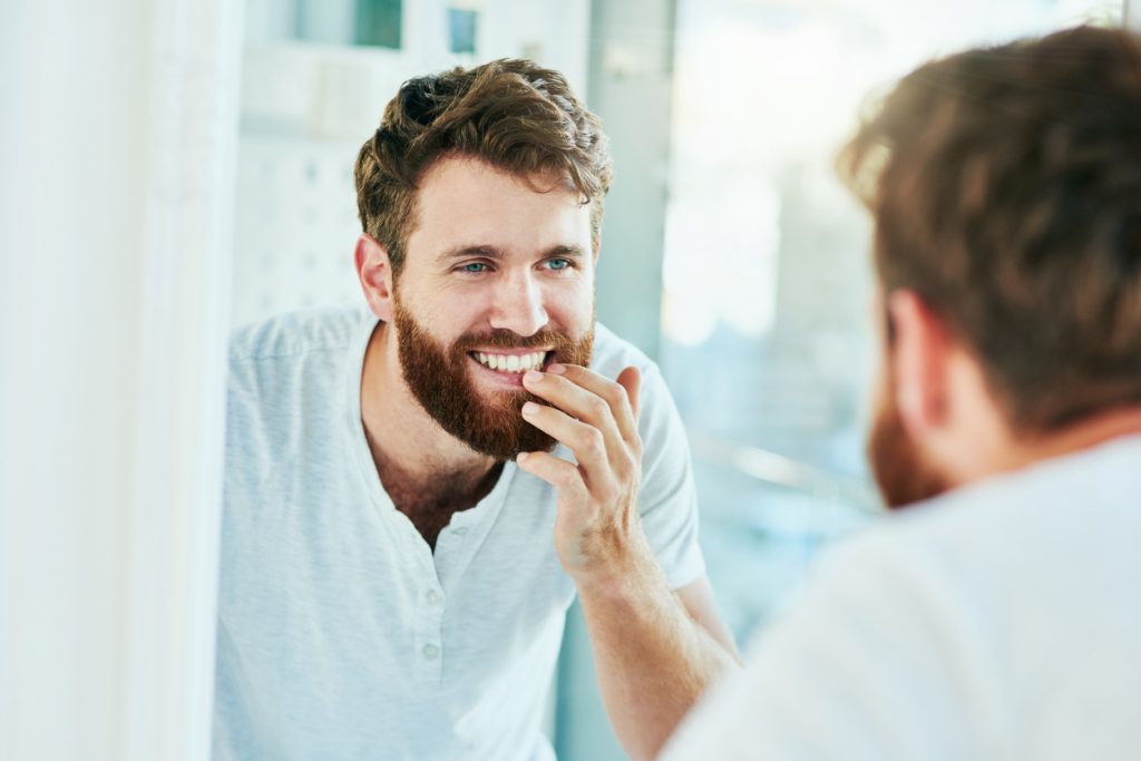 A young man checking his teeth and gums in the bathroom mirror.