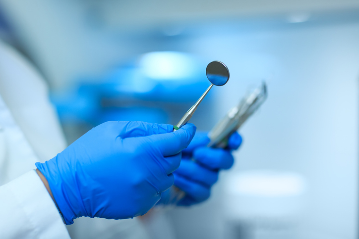 Periodontist holding mirror and periodontal explorer during surgery.